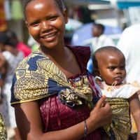 A woman wearing traditional West African dress holding a baby