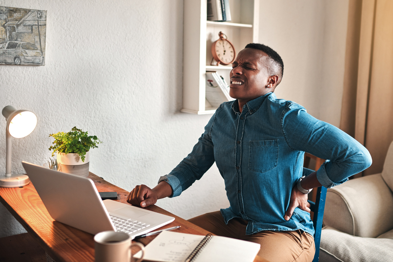 A man on an office chair is clutching his back in pain