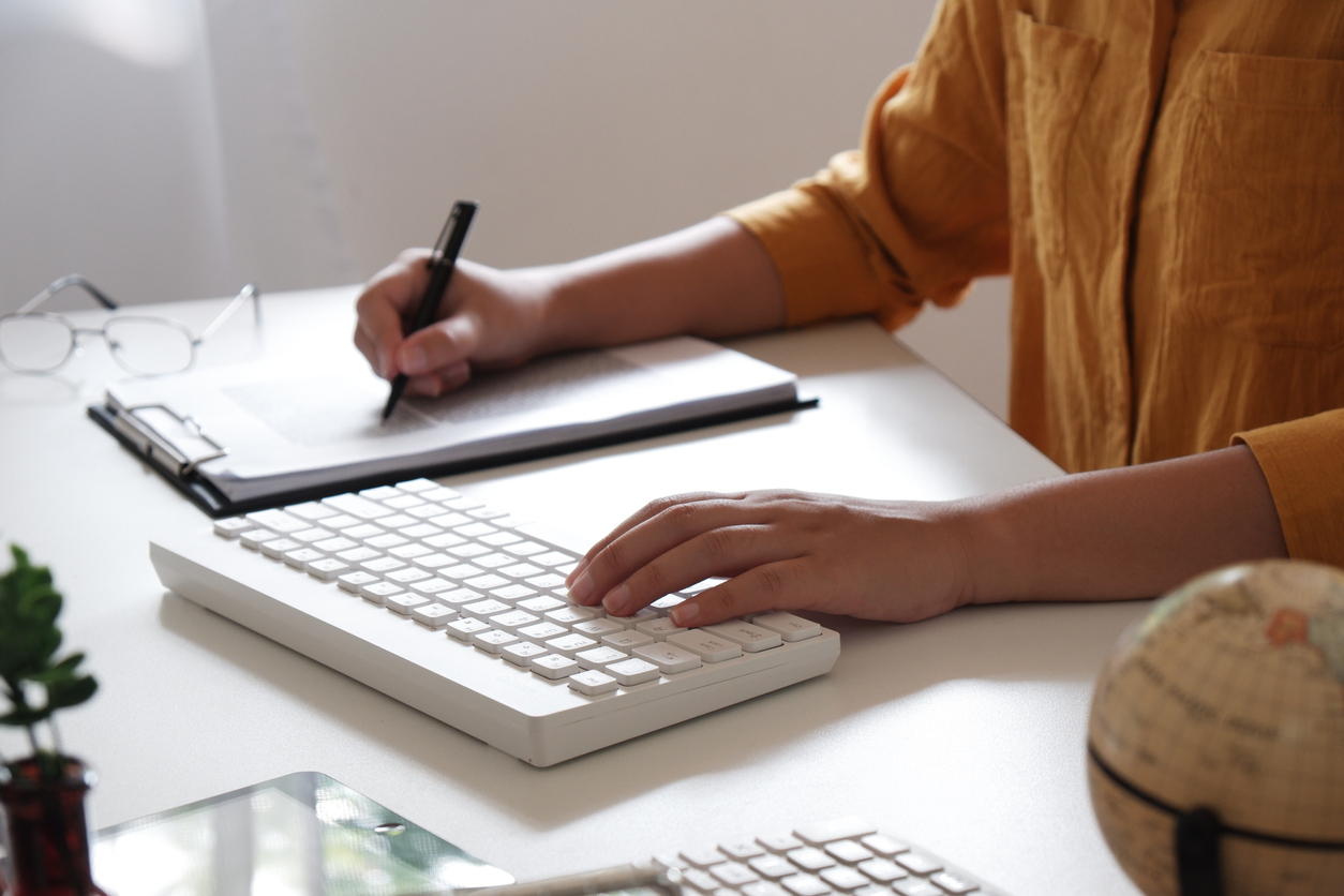 Woman writing in a notepad and typing on a keyboard