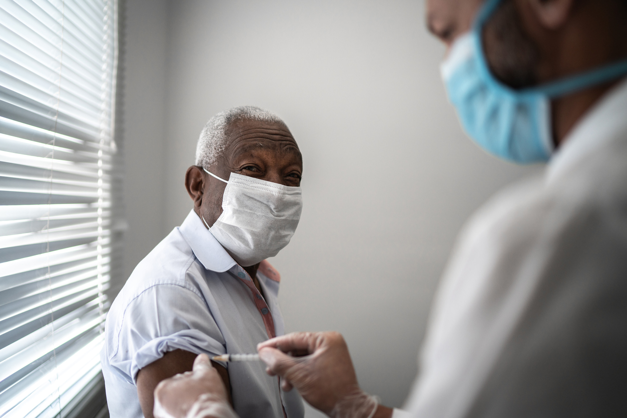 doctor administering a vaccine to an older man, both are wearing facemasks