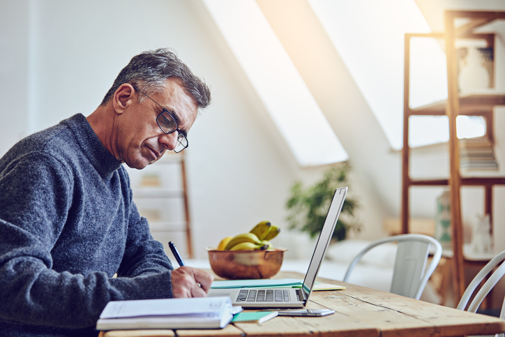 A man writing notes in front of an open laptop