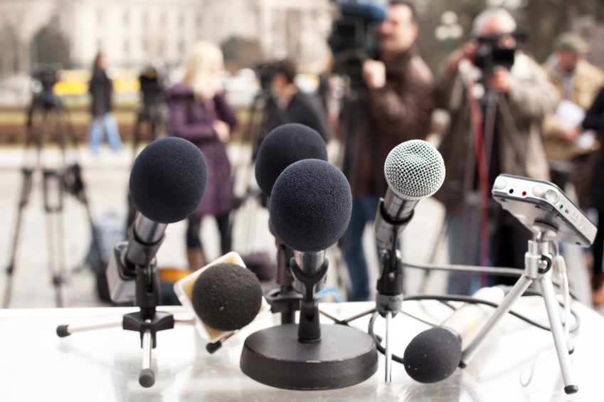 Microphones in the foreground, journalists and cameramen in the background