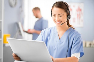 Healthcare professional wearing a headset and on a laptop, she is smiling