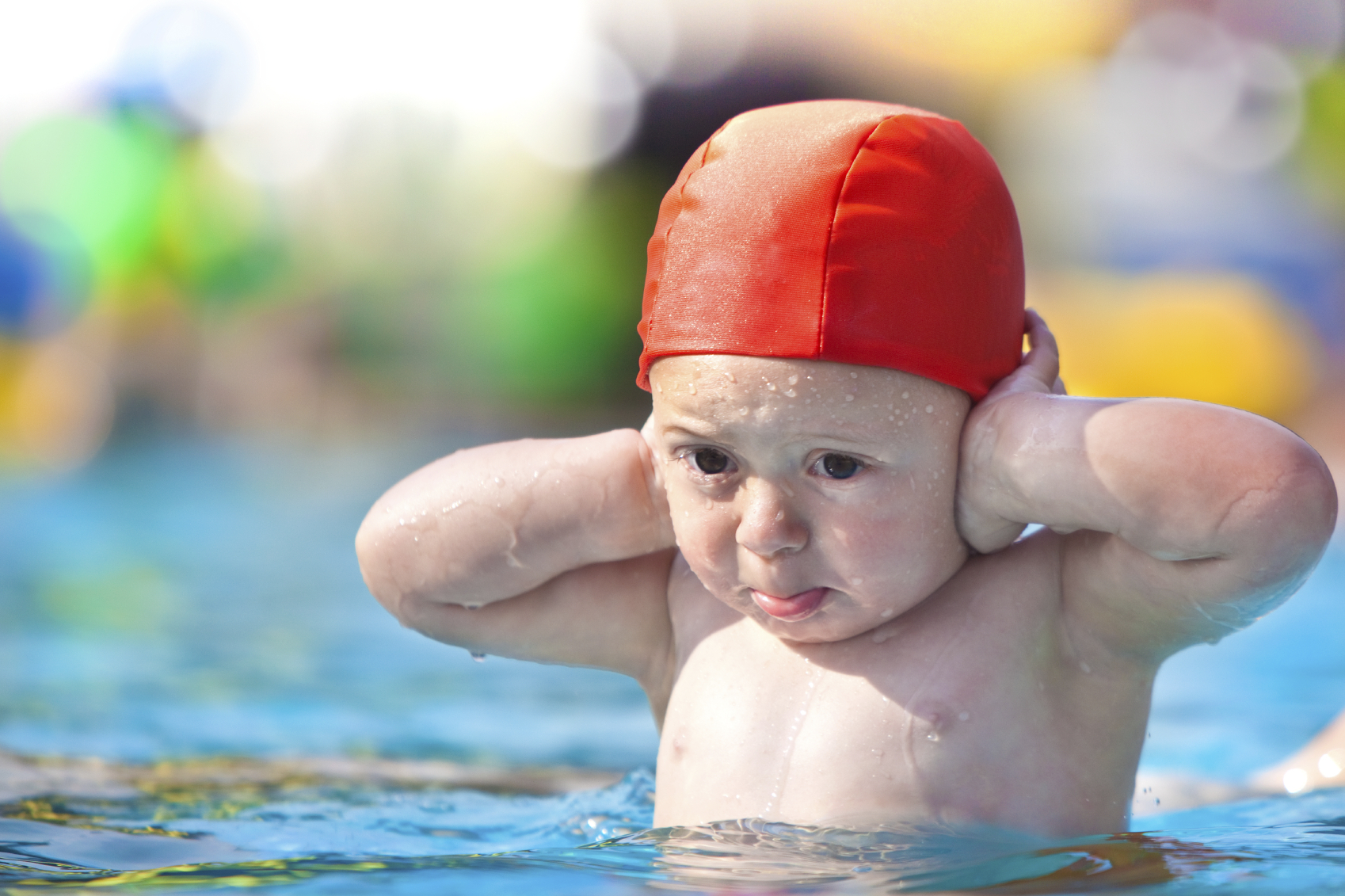A child in a swimming pool with his hands over his ears
