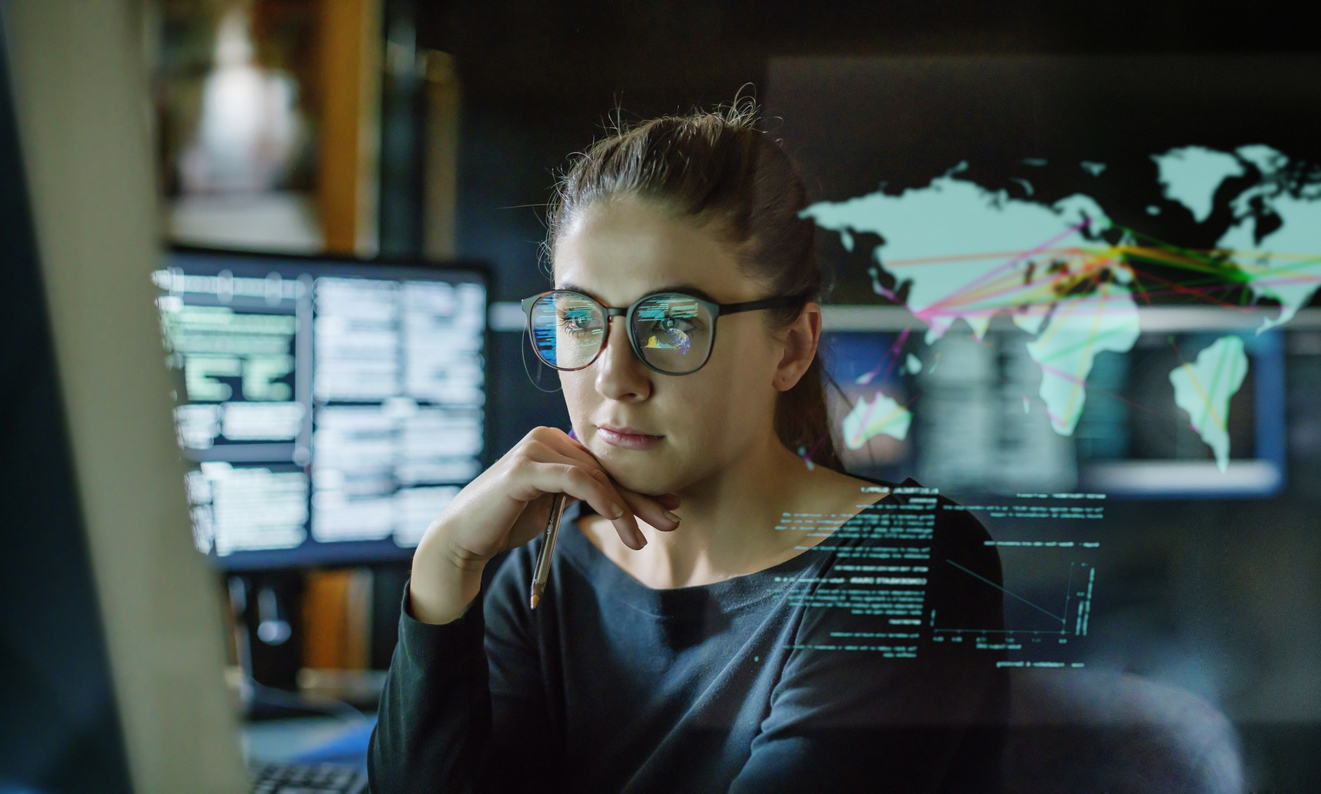 Woman sat a computer, a digital image of the world is overlayed in front of her